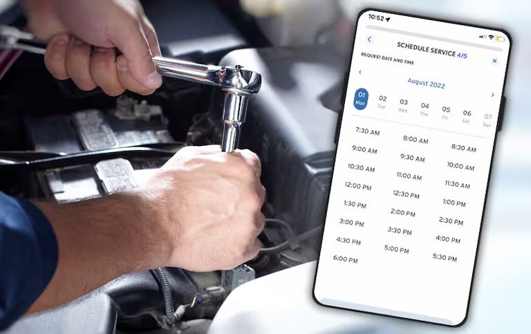 Hands using a wrench on a car engine with a phone screen showing a service scheduling app