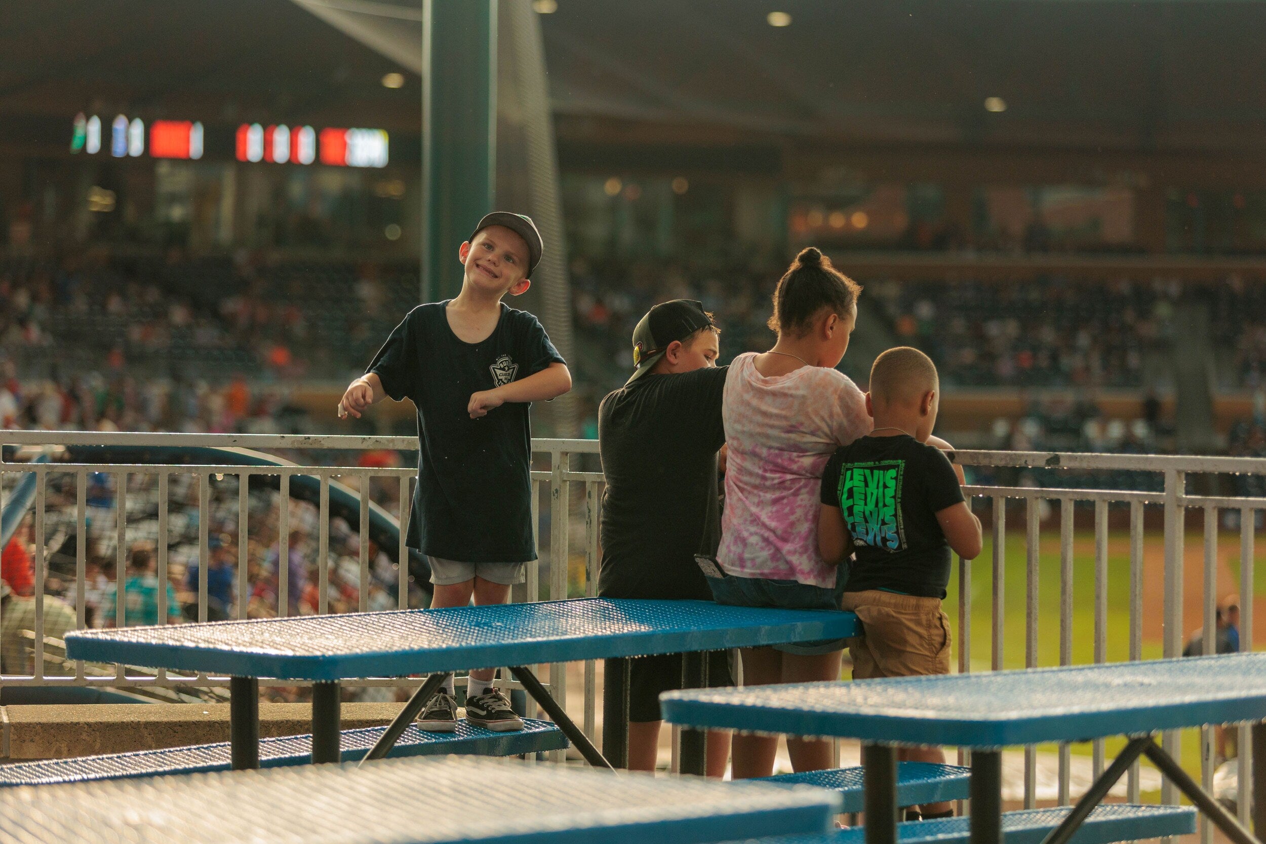 Children standing by a railing at a stadium, watching the field during a game.