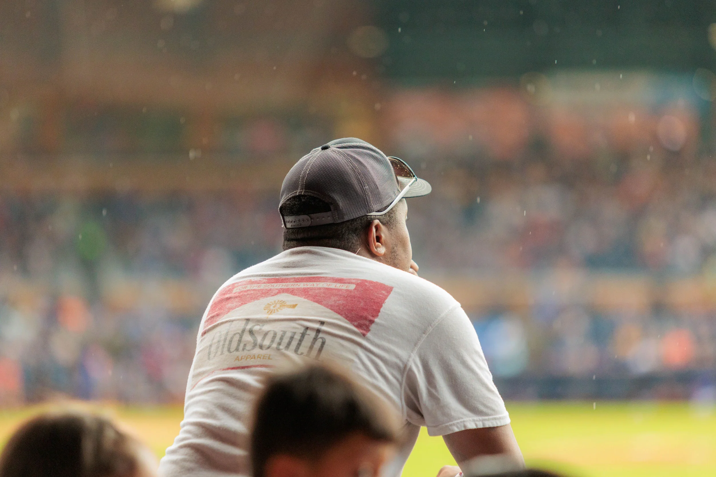 Man in a baseball cap watching a game from the stands.