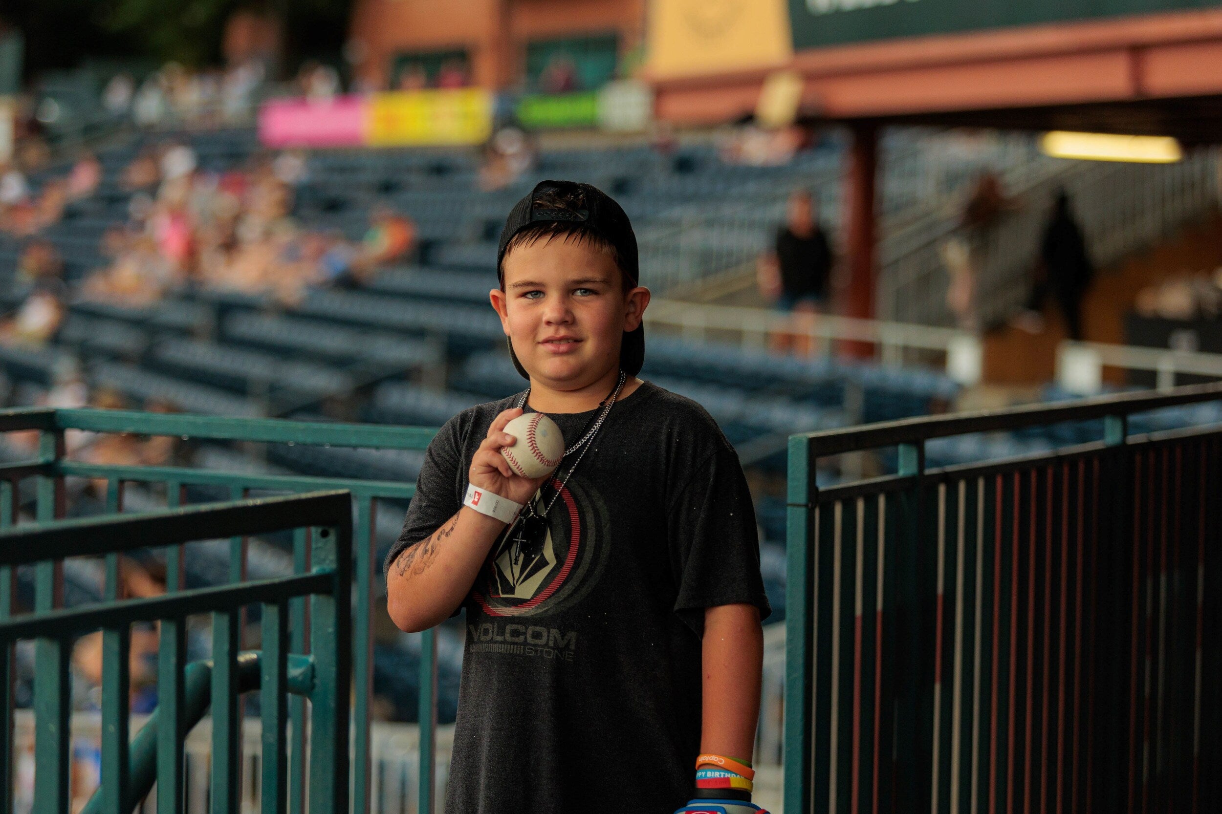 Boy holding a baseball while standing near the seating area of a stadium.